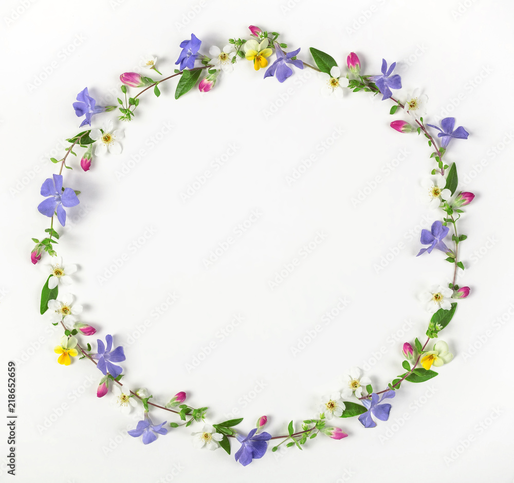 Round frame wreath made of spring wildflowers, lilac flowers, pink buds and leaves isolated on white background. Top view. Flat lay.