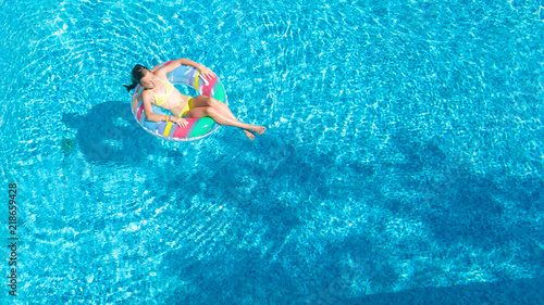 Aerial top view of little girl in swimming pool from above, kid swims on inflatable ring donut , child has fun in blue water on family vacation resort 