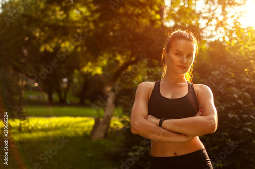 Fototapeta Naklejka Na Ścianę i Meble -  Young sportive woman looking at camera with hands crossed in summer park. Strong happy girl smiling. Healthy lifestyle