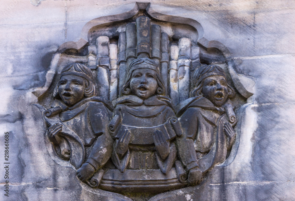 Fototapeta premium Edinburgh, Scotland, UK - June 13, 2012; Closeup of stone mural featuring three singing choir boys with organ pipes behind them. Partly blackened in beige side stone wall of Parliament House.