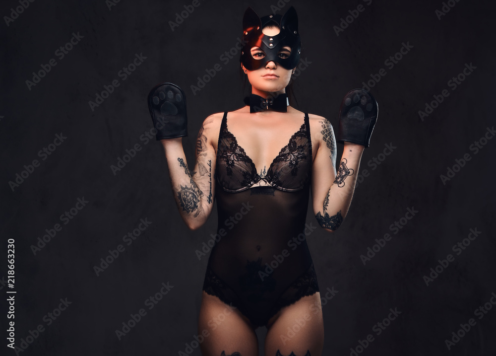 Obraz premium Sexy woman wearing black lingerie in BDSM cat leather mask and accessories posing on dark background. 