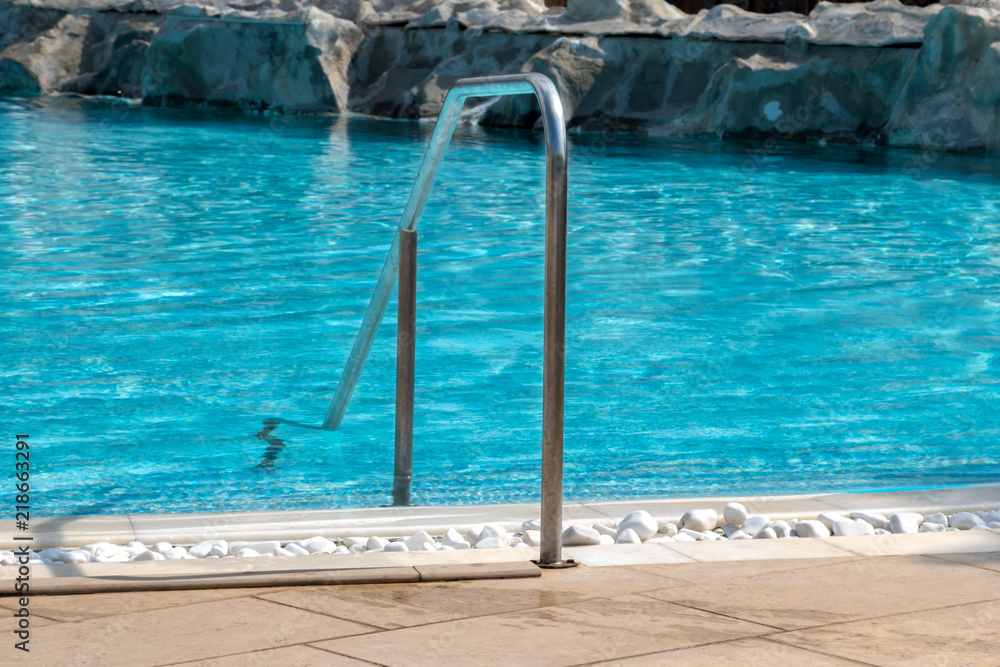 Metal handrail of an empty outdoor pool with decoration of small white rocks.