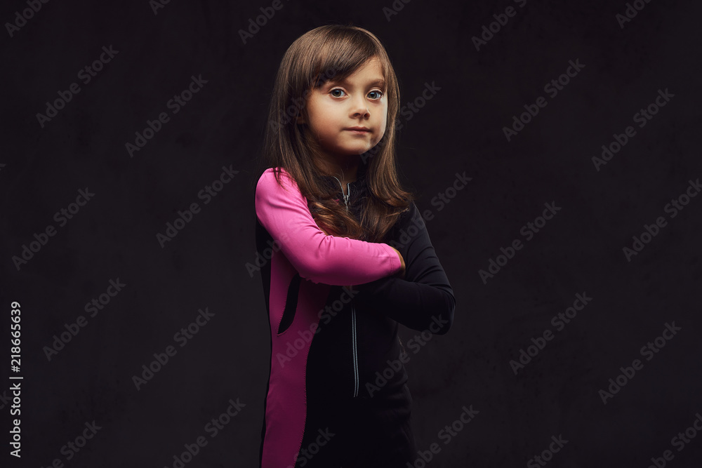 Confident little girl dressed in sportswear standing with crossed arms. Isolated on dark textured background. Confident little girl dressed in sportswear standing with crossed arms. Isolated on dark textured background.