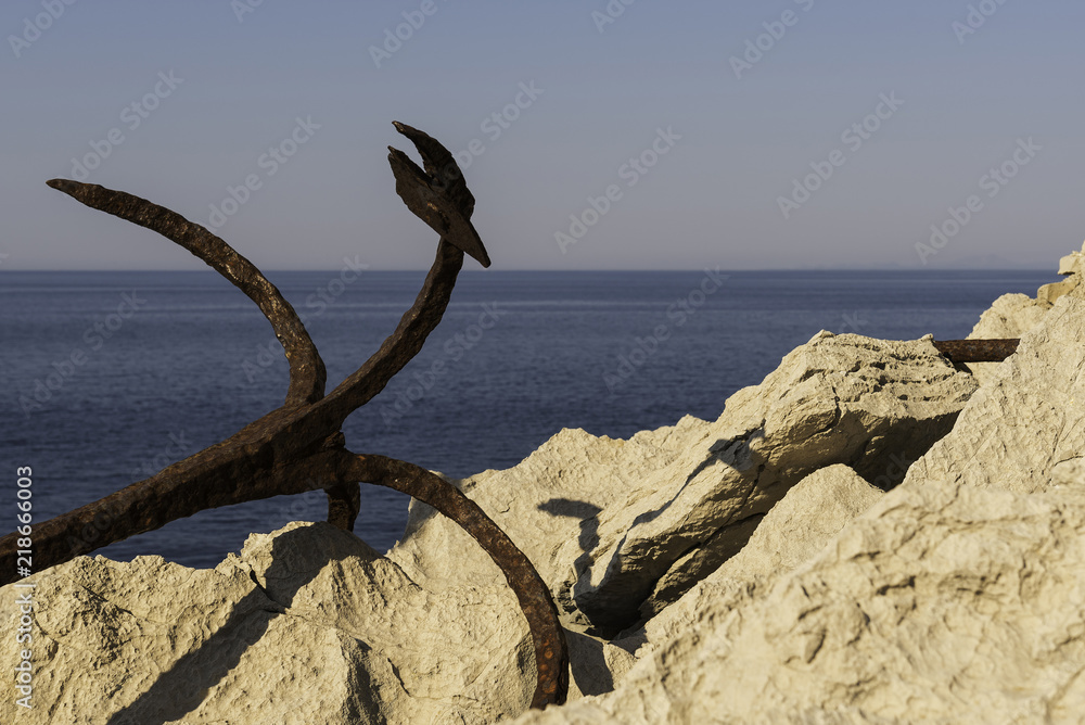 Rusty anchor at the rocky coast