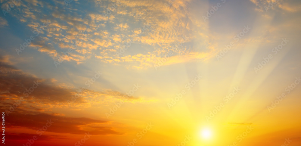 Obraz premium Zachmurzone niebo i jasne słońce wznoszą się nad horyzontem. Szerokie zdjęcie.
