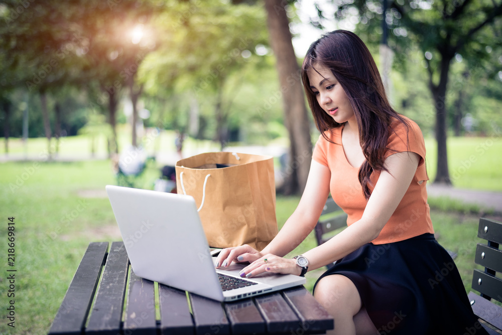 Asian woman using and typing on laptop keyboard in outdoors park. Woman chatting to her friends on social network. People and lifestyle concept. Nature and technology theme. Asian woman using and typing on laptop keyboard in outdoors park. Woman chatting to her friends on social network. People and lifestyle concept. Nature and technology theme.