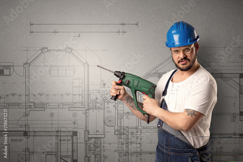 Worker standing with tool in his hand in front of technical drawings. photo