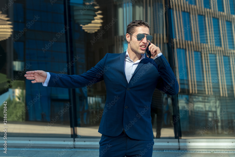 Angry business man in sunglasses talking on cell phone in front of modern building Angry business man in sunglasses talking on cell phone in front of modern building