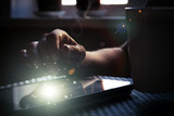 The tablet is in the hands of a woman. Magic glow on the screen of the tablet. Dark background, close-up