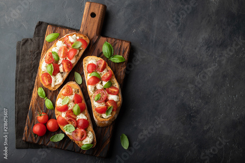 Bruschetta with tomatoes, mozzarella cheese and basil on a cutting board. Traditional italian appetizer or snack, antipasto. Top view with copy space. Flat lay photo