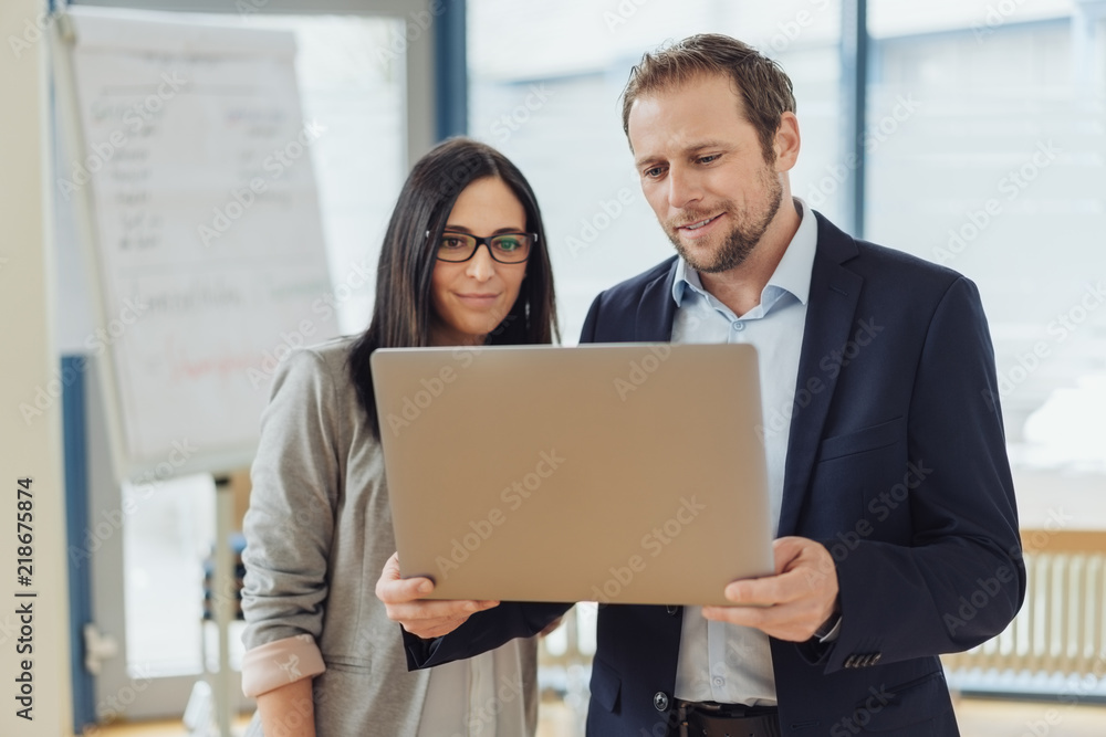 kollegen stehen im büro und schauen gemeinsam auf einen laptop kollegen stehen im büro und schauen gemeinsam auf einen laptop