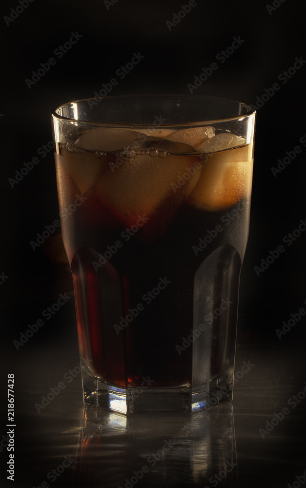 Glass still life image Cola with ice in a glass on a black background Glass still life image Cola with ice in a glass on a black background
