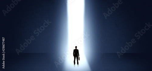 Businessman standing and seeing the light at the end of a big wall  