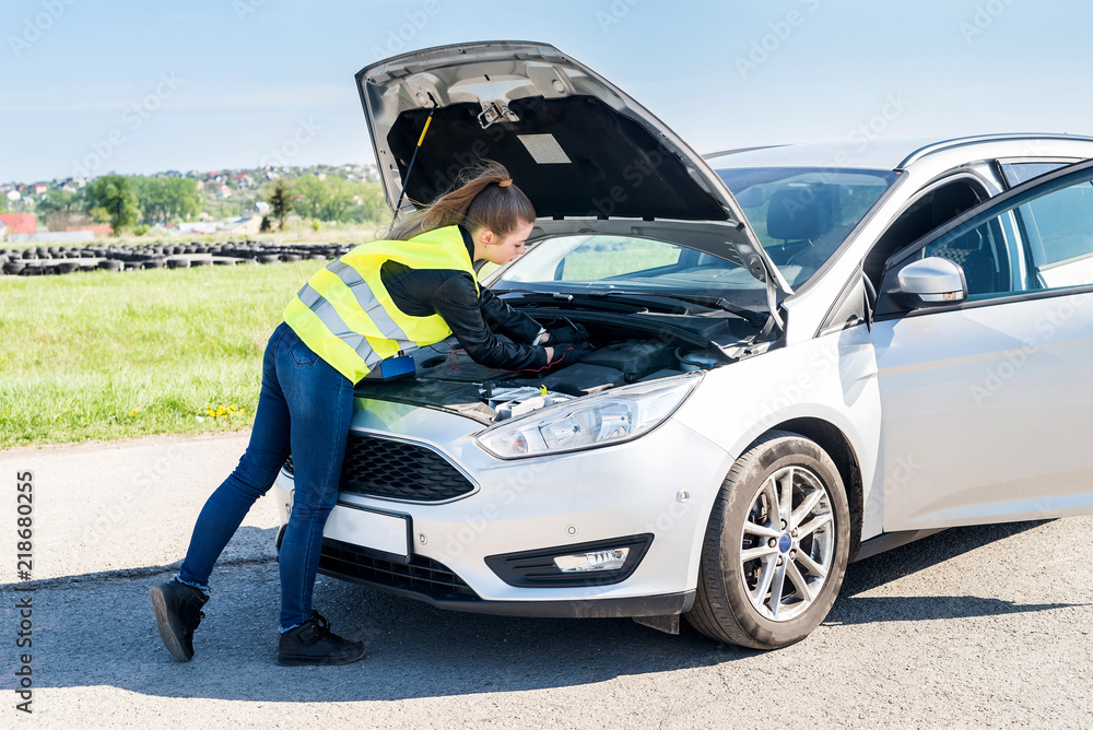 Woman testing car battery in broken car on roadside Woman testing car battery in broken car on roadside