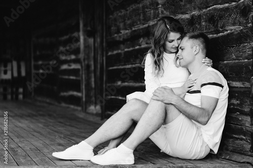 Young pretty couple in love sitting on veranda of old house. Handsome blonde girl in white dress hugging her boyfriend