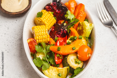 Baked vegetables: pumpkin, beets, carrots, peppers, zucchini and corn in white dish, white background.