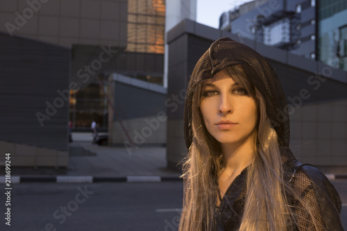 Portrait of a fashion urban girl wear black hood in the cityscape in warm light close up