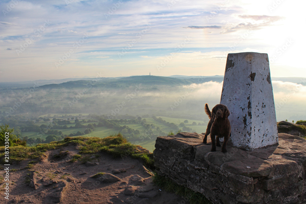 Fototapeta premium Morning view across the countryside at sunrise with fog and clouds of dog and trig point