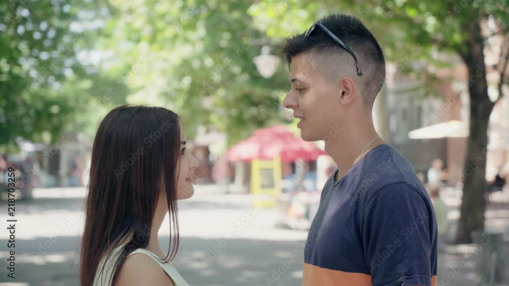 Profile of a young happy couple in love standing, smiling and talking about their emotions and feelings in a green park alley in summer. Profile of a young happy couple in love standing, smiling and talking about their emotions and feelings in a green park alley in summer.