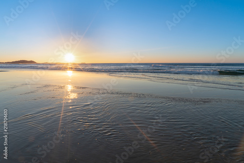 Sunrise star burst over the beach with shiny wet sand in the foreground  NSW  Australia