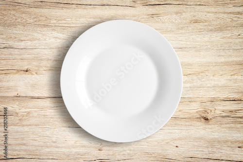 Top view of empty white food plate on a wood background.