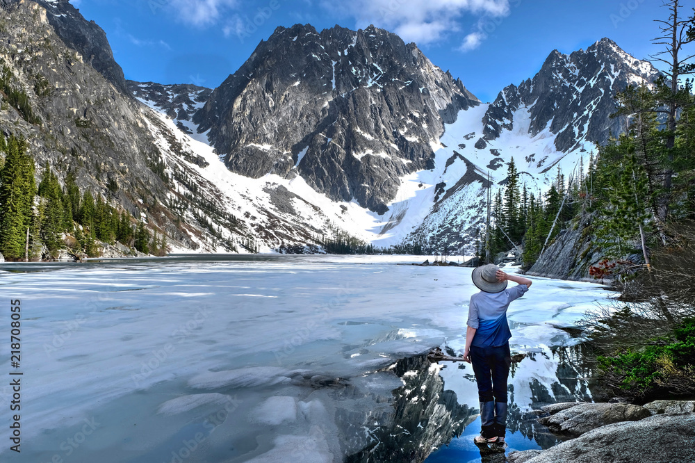 Naklejka premium Hiking in Washington State. Woman stading by beautiful lake covered with ice. Enchantments lakes. Leavenworth. WA. United States of America.