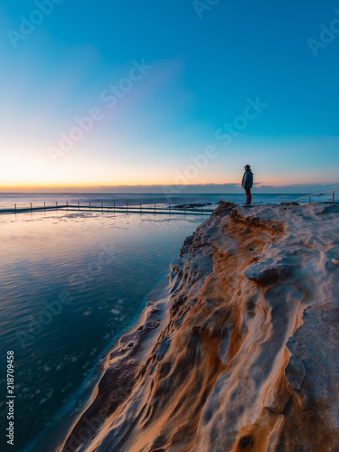 A person standing on the rock cliff facing the ocean.