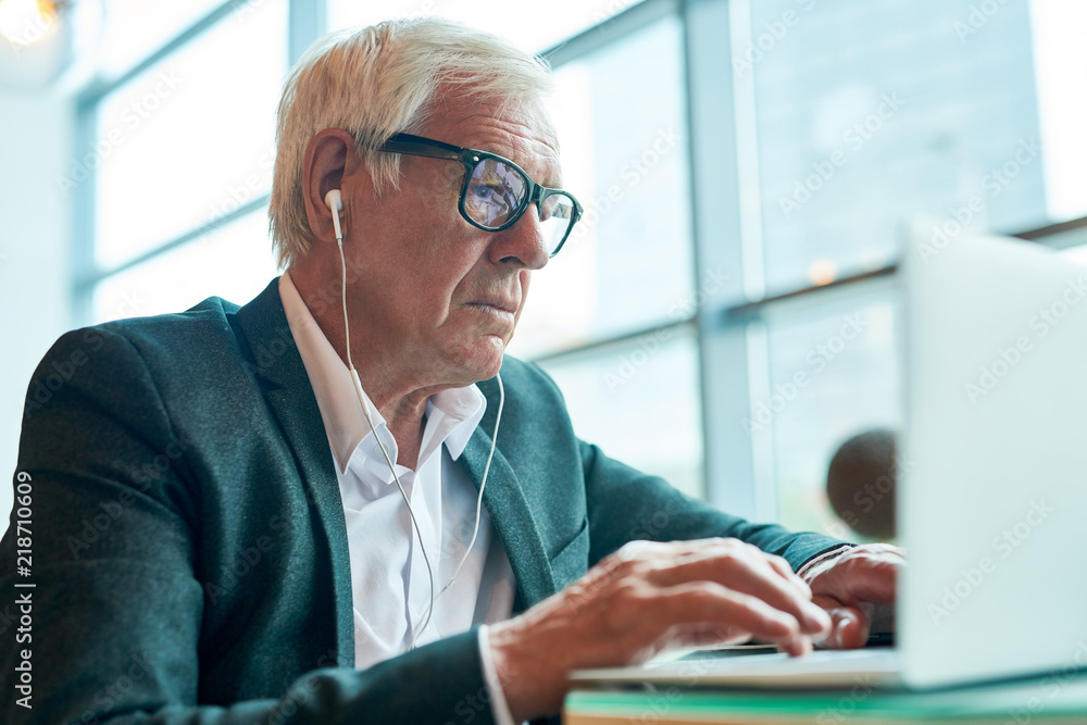 Side view portrait of senior man typing on keyboard while using laptop for browsing internet in cafe, copy space Side view portrait of senior man typing on keyboard while using laptop for browsing internet in cafe, copy space