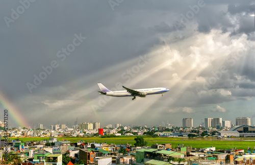 Passenger plane flying through the urban area with sunrays and rainbow in the sky prepared landing airport. Business trip, commercial plane, travel