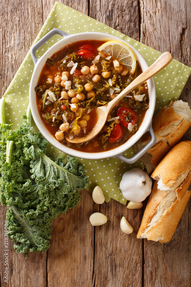 Soup of chickpeas, kale, tomatoes, garlic and potatoes with lemon close up on the table. Vertical top view Soup of chickpeas, kale, tomatoes, garlic and potatoes with lemon close up on the table. Vertical top view