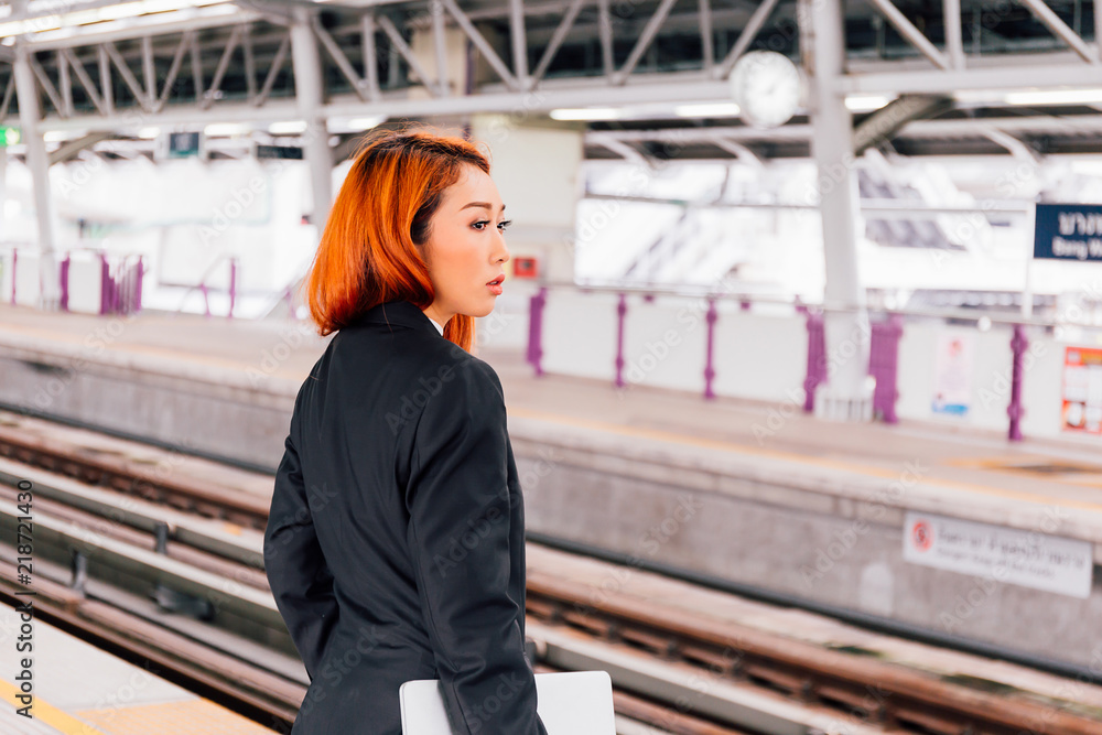 Young beautiful Asian businesswoman holding a laptop and waiting for the train to arrive.