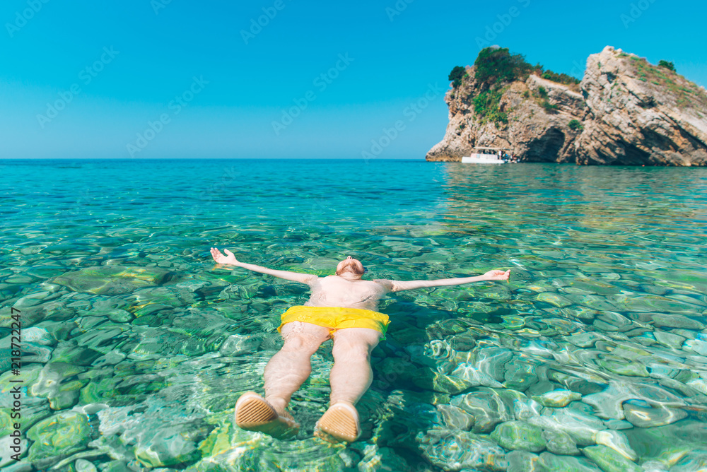 man laying at back in transparent clear water with rocky bottom