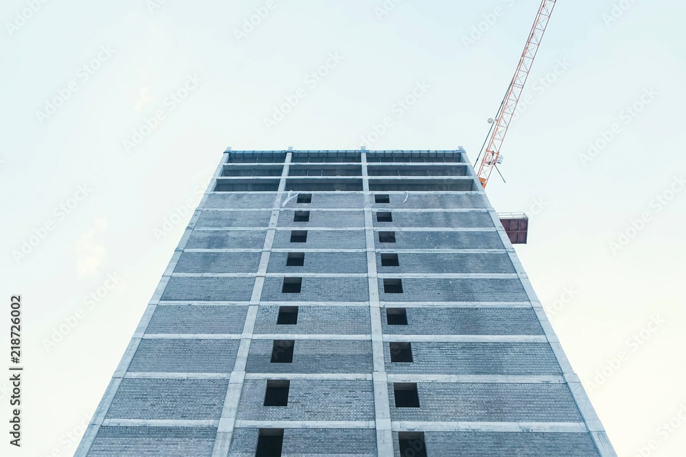 Multi-storey under construction building and construction crane on the background of clear sky. Multi-storey under construction building and construction crane on the background of clear sky.