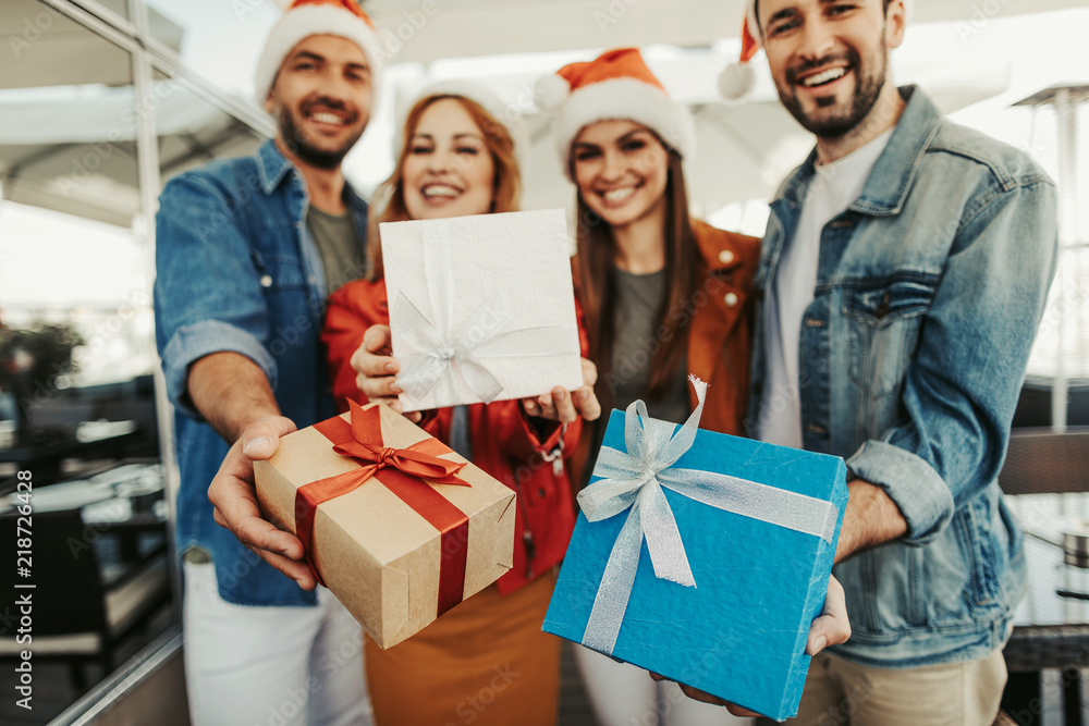 Merry Christmas. Close up of beautiful gift boxes with ribbons. Smiling group of people in Santa Claus hats on blurred background Merry Christmas. Close up of beautiful gift boxes with ribbons. Smiling group of people in Santa Claus hats on blurred background