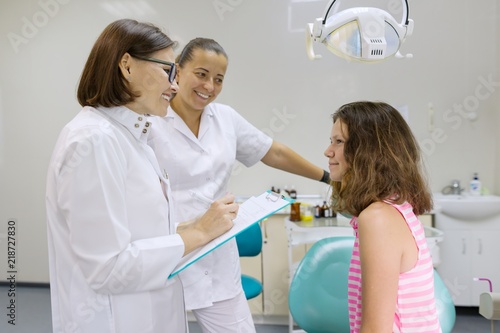 Teenage girl is sitting in a dental chair talking to female dentists.