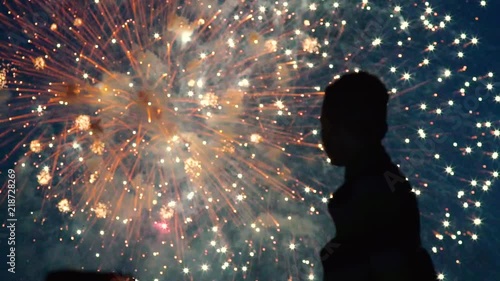 Silhouette of boy who watch the fireworks in the night sky. Bright and colorful lights in the sky. A beautiful sight is watched by the guy. Red, green and orange lights in the blue sky