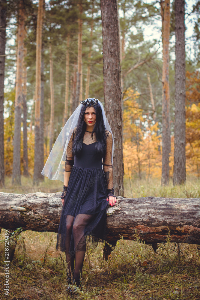 Halloween Witch in a dark forest. Beautiful young woman in witches modern dress . Halloween art design. Dark theme For Halloween Concept Halloween Witch in a dark forest. Beautiful young woman in witches modern dress . Halloween art design. Dark theme For Halloween Concept