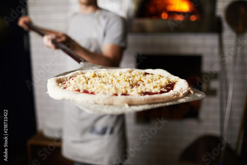 Metallic spade or tray with raw pizza held by baker before putting it into oven