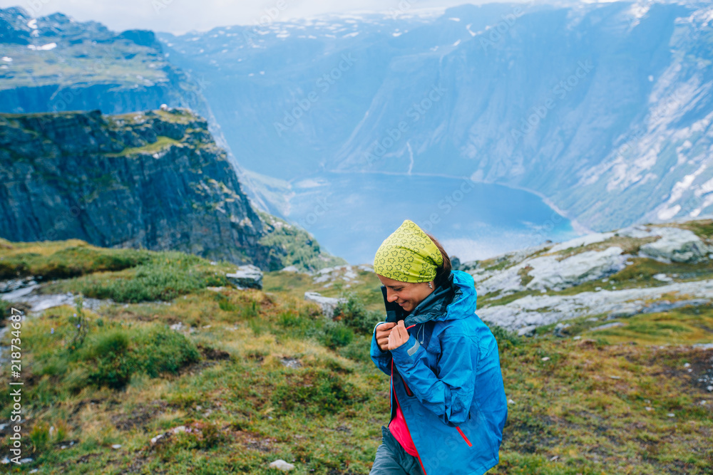 Happy woman zip up and wrapping in blue sportive jacket before rain, get ready for adventure and smiling in cliff during trip Norway. Trolltunga hiking route