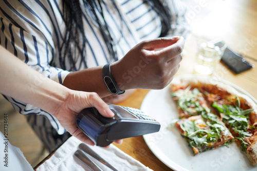 Payment machine in hand of waiter and that of client with smartwatch over it