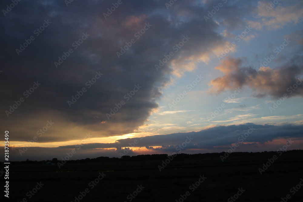 Dark clouds with several sunbeams during sunset in colorful sky in the Netherlands.