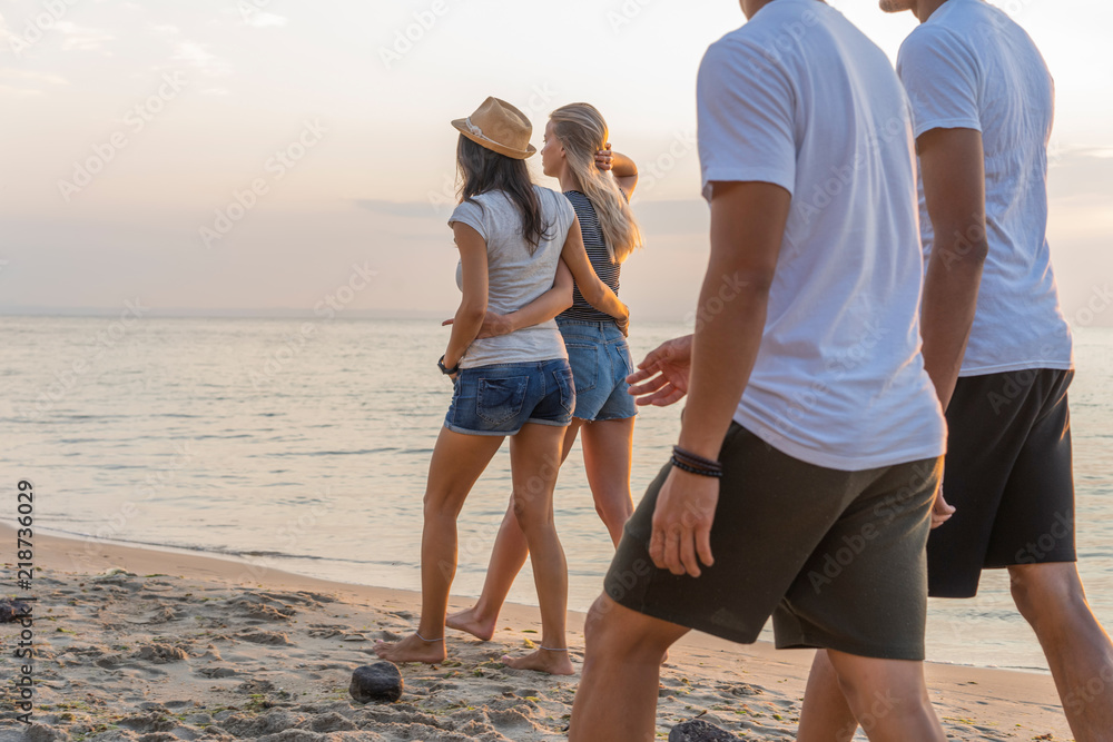 Group of friends walking along a beach at summertime. Happy young people enjoying a day at beach Group of friends walking along a beach at summertime. Happy young people enjoying a day at beach