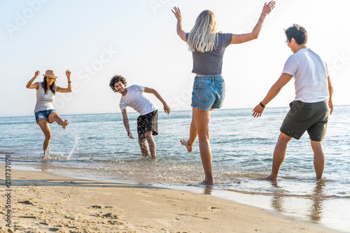 Group Of Friends Run Through Waves Together On Beach Vacation.