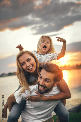 Portrait of happy unshaven husband spending tie with cheerful wife and satisfied female child in nature