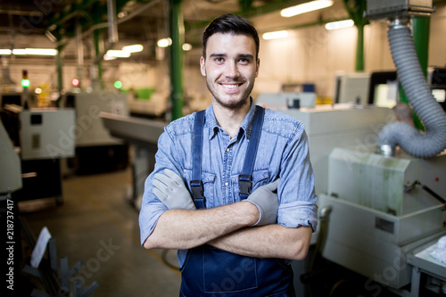 Portrait of young engineer with arms crossed smiling at camera while standing in factory