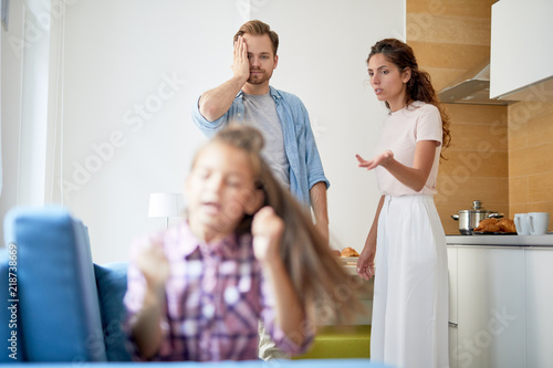 Young woman complaining on naughty little daughter to her husband while pointing at the girl