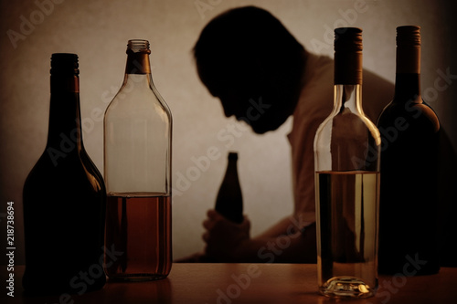 Fotografie silhouette of a person drinking behind bottles of alcohol with added filter