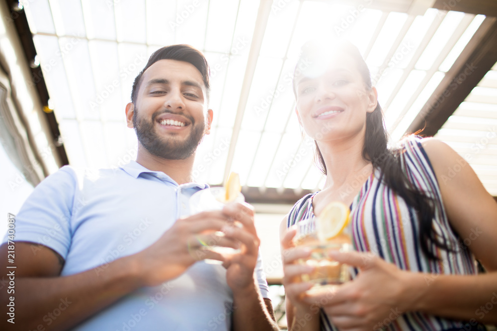 Young smiling man and his girlfriend with drinks looking at camera on sunny day while enjoying their date Young smiling man and his girlfriend with drinks looking at camera on sunny day while enjoying their date