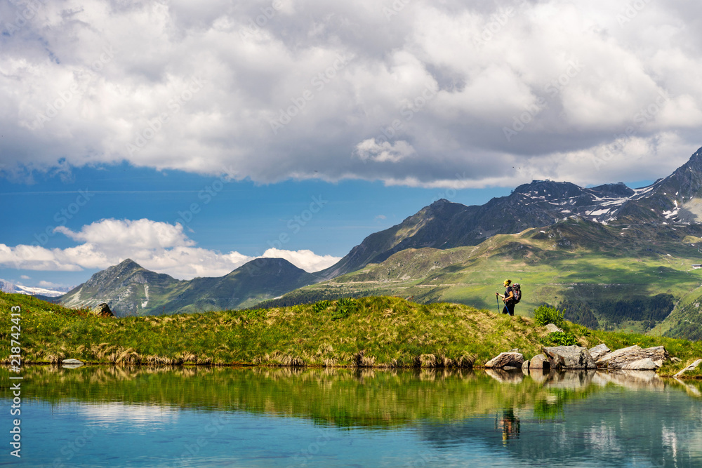 Female traveler with backpack hiking mountain trail next to a mountain lake and admiring views of Swiss Alps in Val de Bagnes area, Switzerland.
