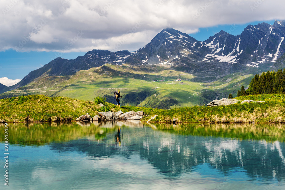 Obraz premium Female traveler with backpack hiking mountain trail next to a mountain lake and admiring views of Swiss Alps in Val de Bagnes area, Switzerland.